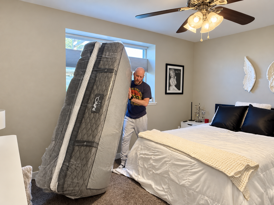 Stephen Meyer carrying a folded, plastic-wrapped mattress inside a customer's bedroom.